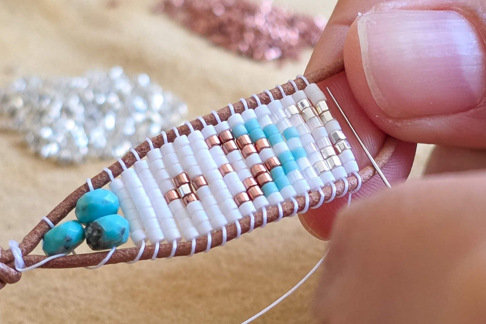 Close-up of hands working on a beaded bracelet with turquoise beads on a smoked buckskin surface